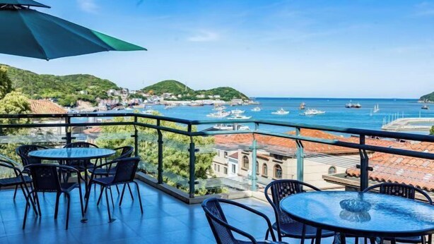 A balcony with round tables and chairs, overlooking a coastal area with boats and buildings. - Chaoqibanpo (Zhoushan)