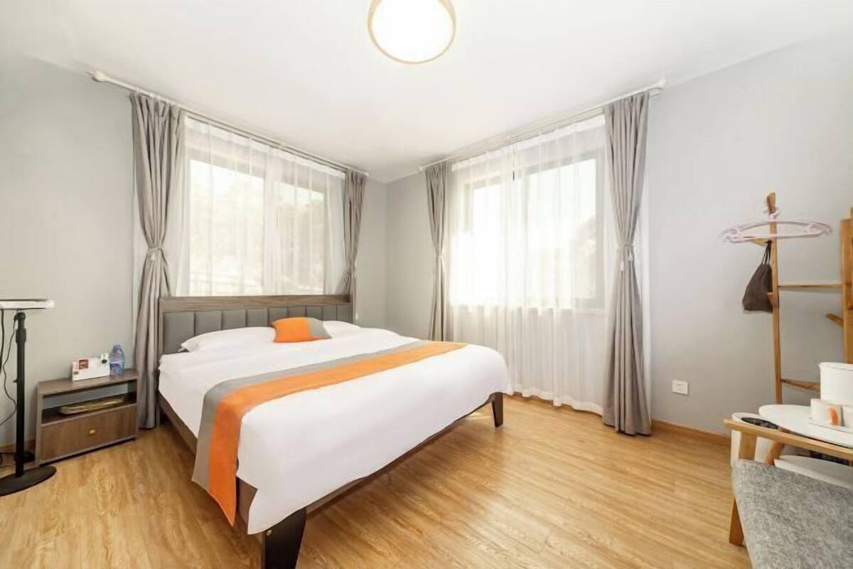 A hotel room with a bed, a desk, a chair, a coat rack, and a window with curtains.