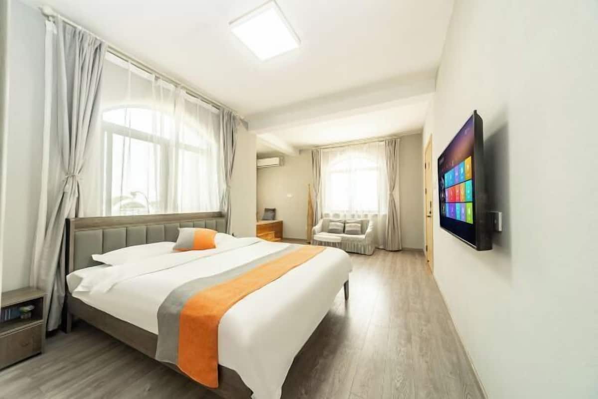 A hotel room with a large bed, a TV mounted on the wall, and a seating area with a sofa and armchairs.