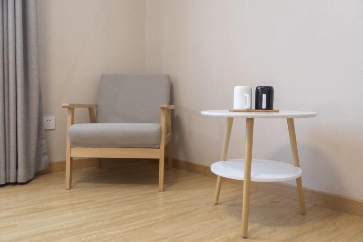 A room with a wooden floor, a grey upholstered chair, and a small white table with a black object on it.