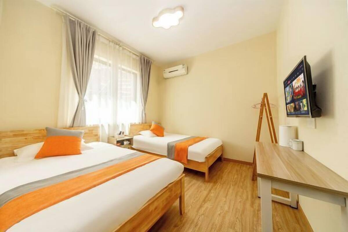 A hotel room with two beds, a wooden desk, a television, and an air conditioning unit.
