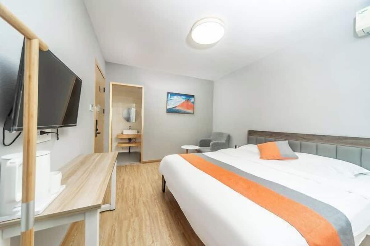 A hotel room with a bed, a desk, a television, a painting, and a bathroom.