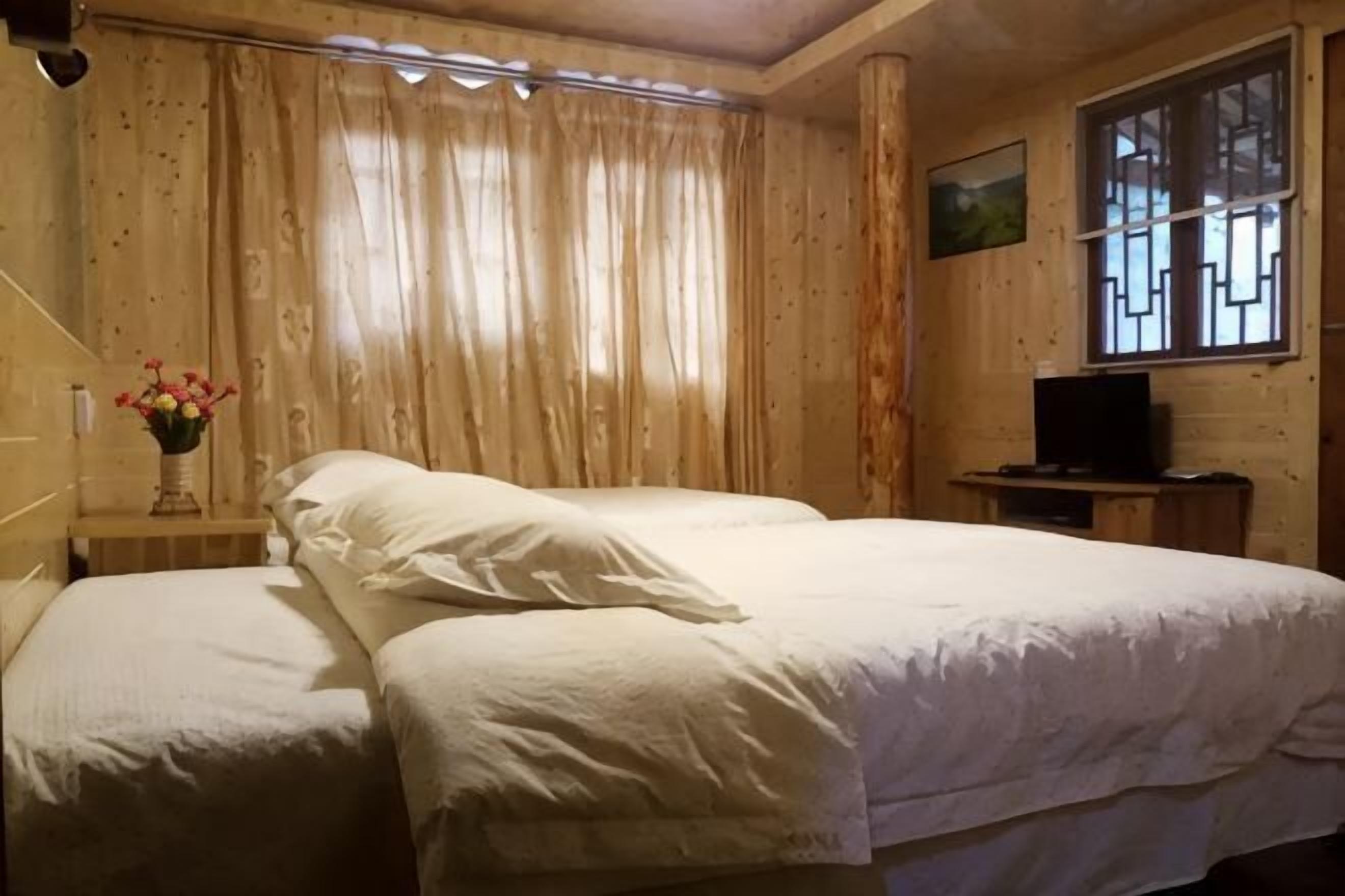 A room with two beds, a television on a wooden stand, a window with a view, and a painting on the wall.