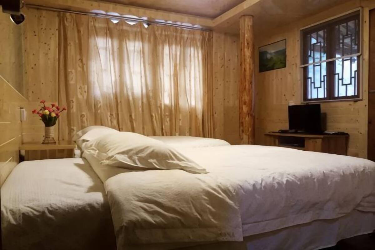 A room with two beds, a television on a wooden stand, a window with a view, and a painting on the wall.
