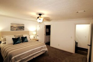 A bedroom with a bed, a ceiling fan, a nightstand, a lamp, and a painting on the wall.