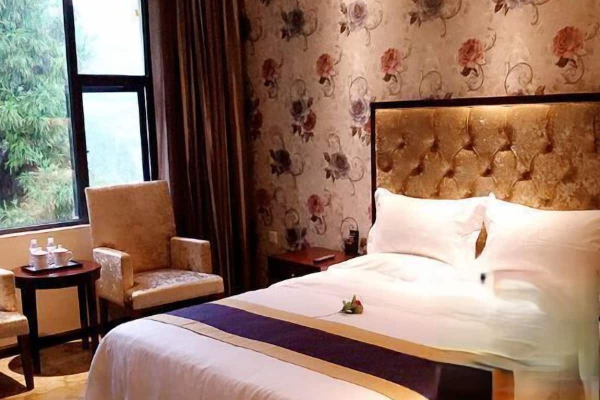 Quarto de hotel com cama, cadeira, mesa de cabeceira e janela com cortinas.