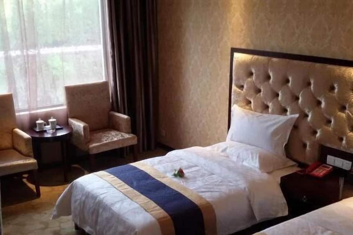 Quarto de hotel com uma cama grande, duas poltronas, uma mesinha com bule e xícaras, e uma janela com cortinas.