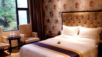 A hotel room with a large bed, two chairs, a small table, and a window with a view of trees.