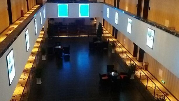 Un vestíbulo de hotel con un espacio central abierto, varias zonas de estar y cuadros enmarcados en las paredes.