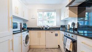 Une cuisine moderne avec des meubles blancs, un lave-linge encastré et une grande fenêtre qui laisse entrer la lumière naturelle.