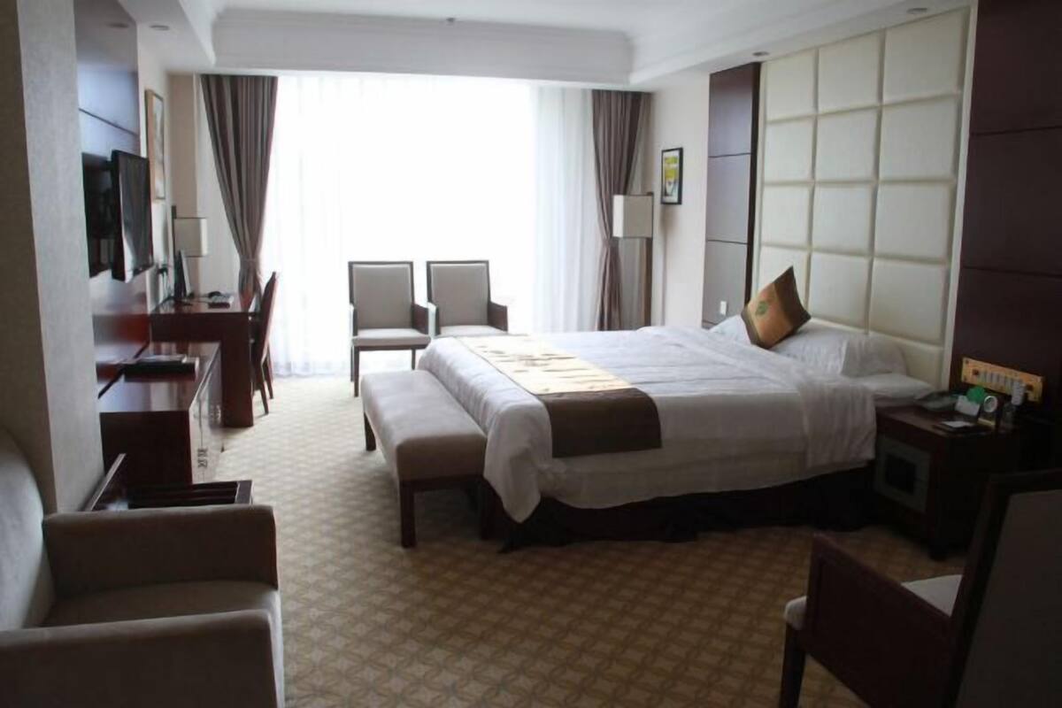 Une chambre d’hôtel avec un grand lit, deux fauteuils, un bureau et une télévision.