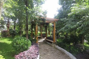 Ein Gartenpfad führt zu einer hölzernen Pergola, umgeben von üppigem Grün.