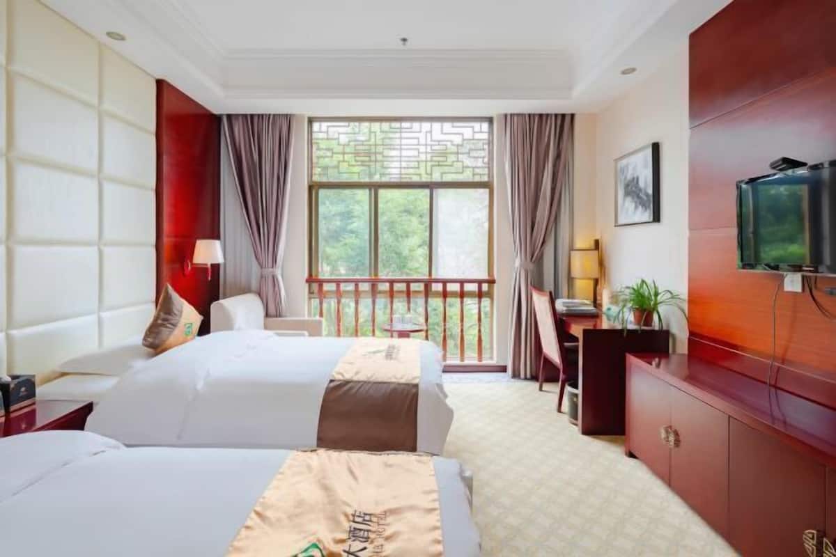 Une chambre d’hôtel avec deux lits, un bureau, une télévision et un balcon donnant sur un espace verdoyant.