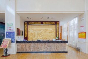 Uma área de recepção com balcão de mármore, parede decorativa e cartazes informativos.