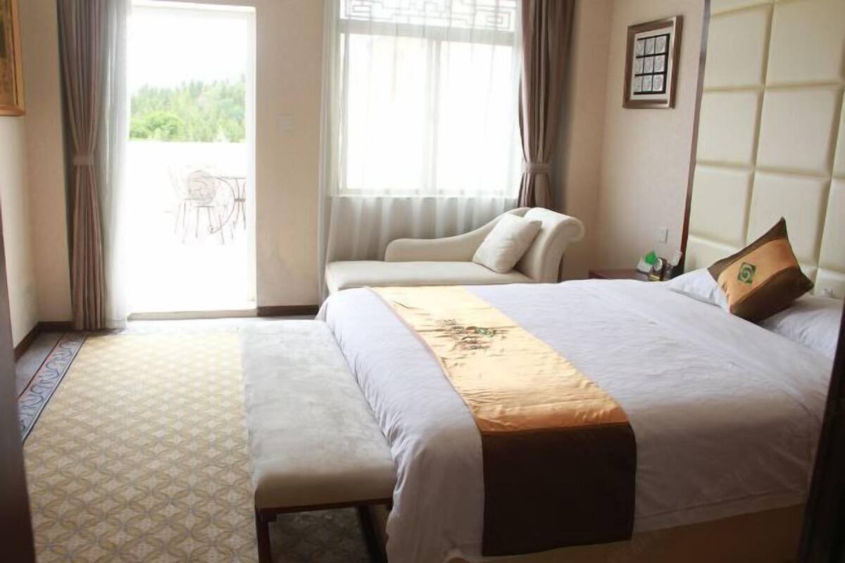 Une chambre d’hôtel avec un lit, un banc, une fenêtre avec des rideaux et une vue sur la verdure à l’extérieur.