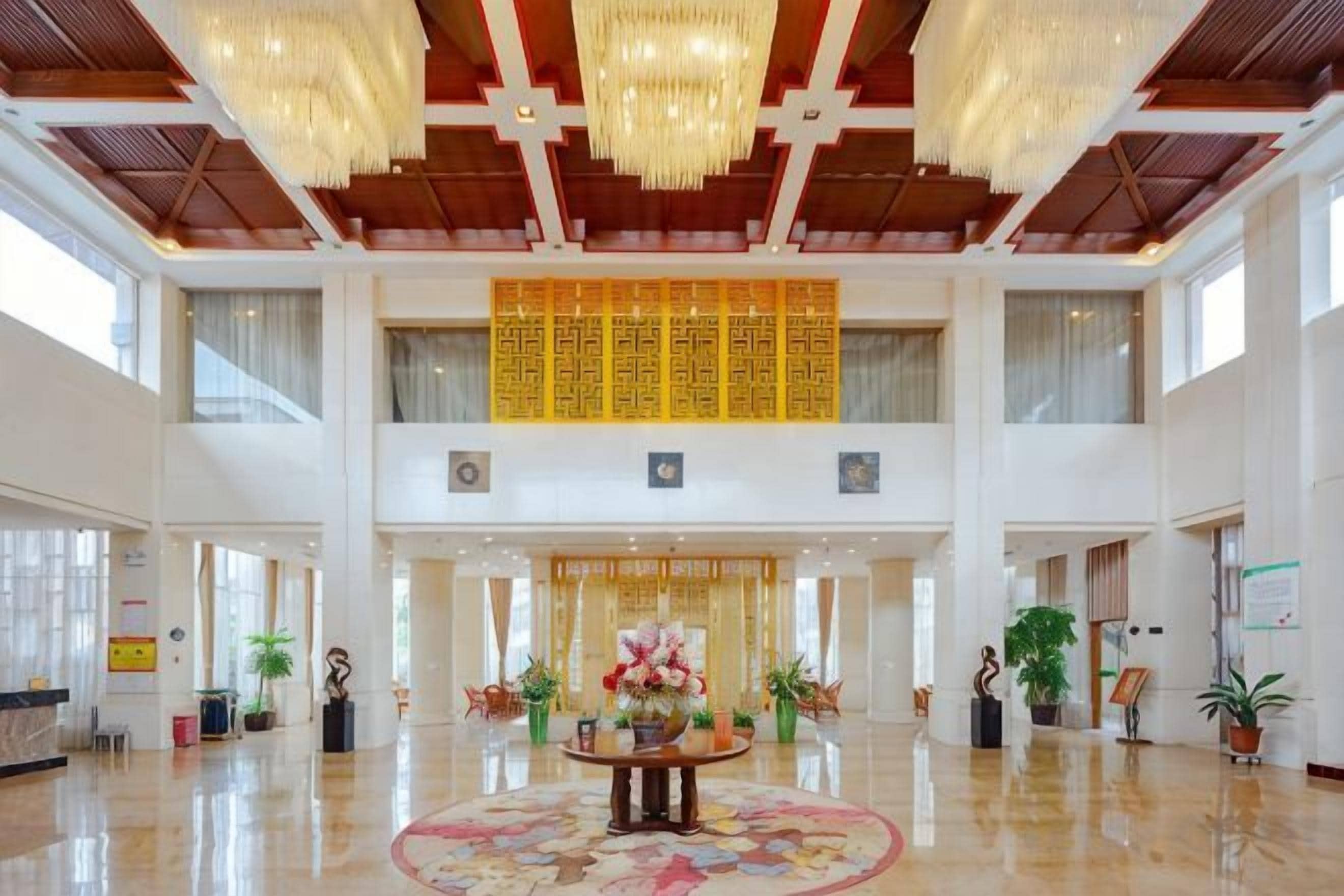 A spacious lobby with a high ceiling, chandeliers, a reception desk, and a large decorative panel.