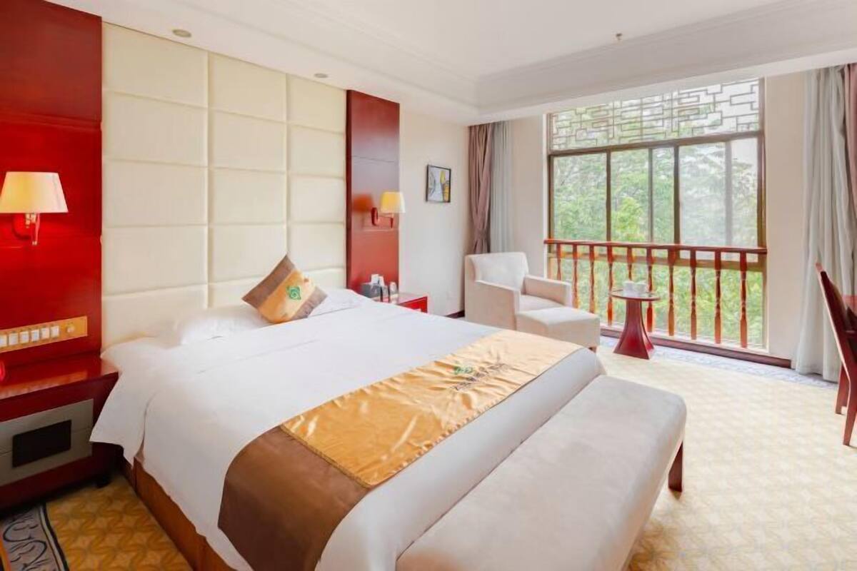 Une chambre d’hôtel avec un grand lit, une petite table, une chaise et un balcon doté d’une balustrade.