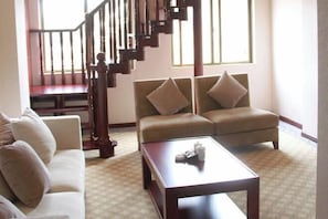 A living room with a sofa, two armchairs, a coffee table, and a staircase.