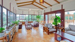 A spacious room with large windows, wooden beams, and a variety of seating arrangements. - Donghe Hotel (Shuangbai)