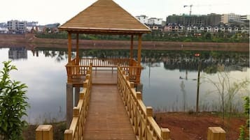 Un belvédère en bois, doté d’un toit et de balustrades, est installé sur une terrasse en bois qui s’étend au-dessus d’une étendue d’eau calme.