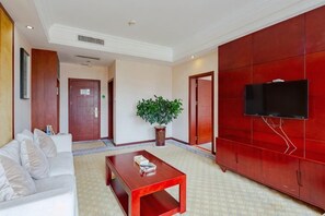 Un hall de hotel con una pared roja, un televisor de pantalla plana montado en ella, un sofá blanco, una mesa de centro de madera y una planta en maceta.
