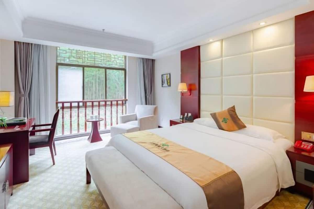 Une chambre d’hôtel avec un grand lit, un bureau avec une chaise, une petite table et un balcon doté d’une rambarde.