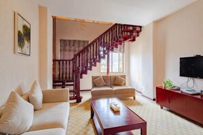 A living room with a staircase, a sofa, a coffee table, and a television.