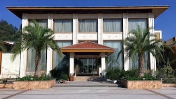 Un edificio moderno con entrada central, grandes ventanales y un área cubierta con palmeras.