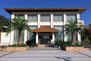 A modern building with a central entrance, large windows, and a covered area with palm trees.