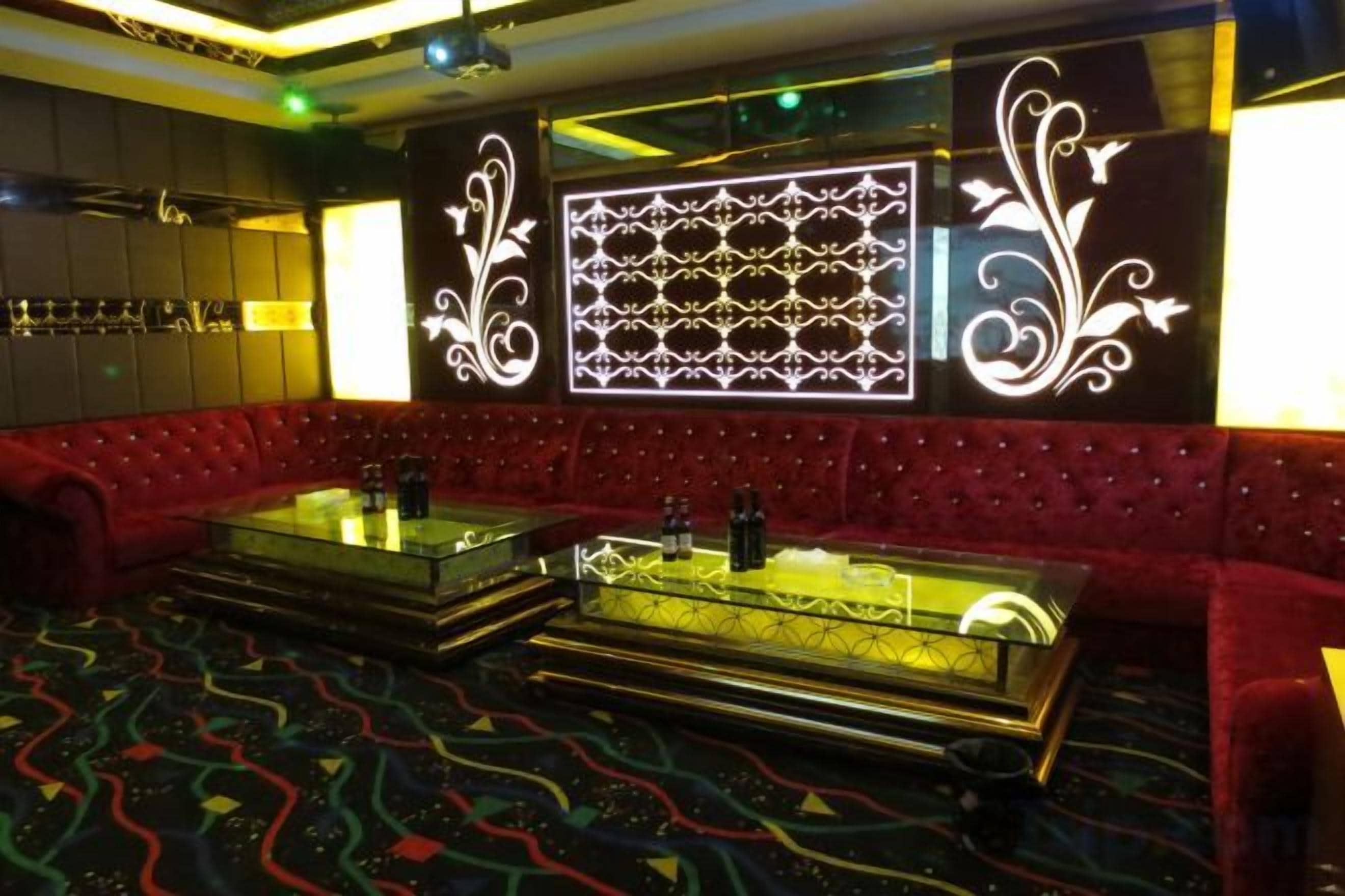 A red upholstered seating area with a patterned wall and a glass coffee table.
