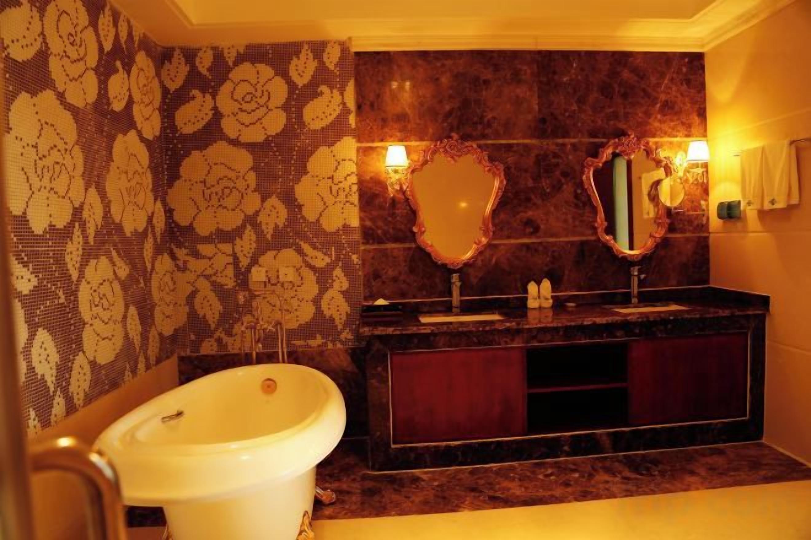 A bathroom with a bathtub, a vanity with a mirror, and patterned wallpaper.