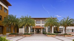 A hotel entrance with a central building, palm trees, and a paved courtyard. - Donghe Hotel (Shuangbai)