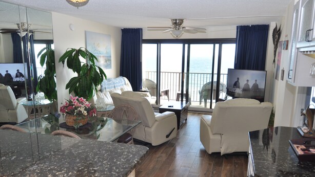 A modern living room with a glass dining table, white sofas, a large potted plant, and a television.