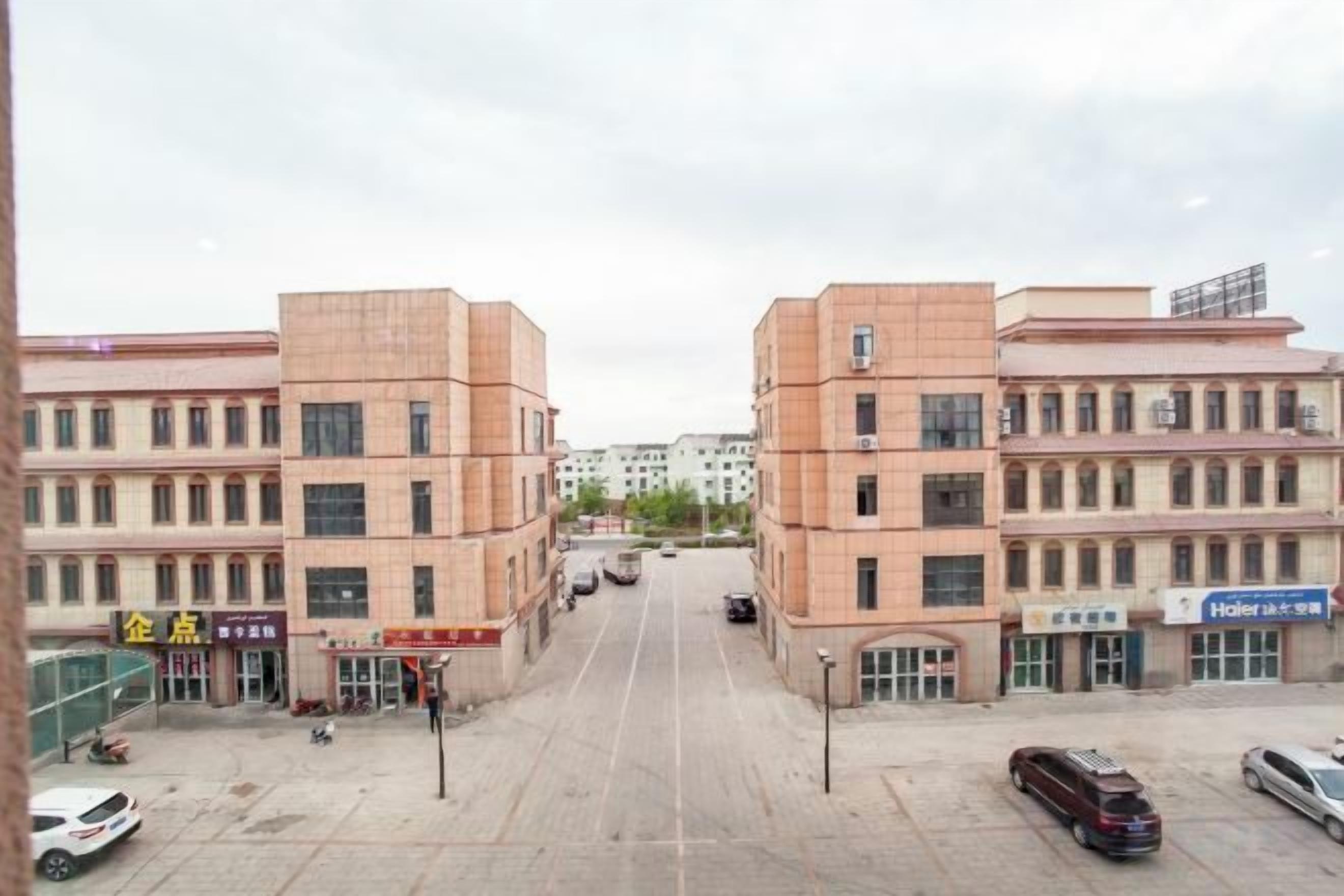 Un immeuble à plusieurs étages doté d’une cour intérieure, sur lequel on peut voir une enseigne d’hôtel et quelques voitures garées.