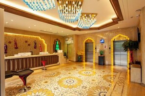 A hotel lobby with a reception desk, a chandelier, a patterned floor, and an elevator.