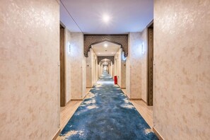 A long, narrow hallway with a patterned carpet, wooden doors, and a fire extinguisher on the right. - Konghe Yizhan Culture Hotel (Turpan)
