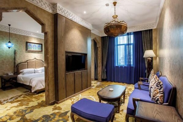 A hotel room with a bed, a TV, a sofa, a table, and a patterned carpet.