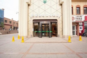 Entrada de hotel con puerta giratoria, pavimento adoquinado y conos de tráfico amarillos.