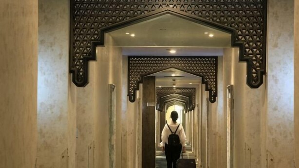 Un couloir aux murs et au plafond ornés de motifs, qui mène à une pièce.