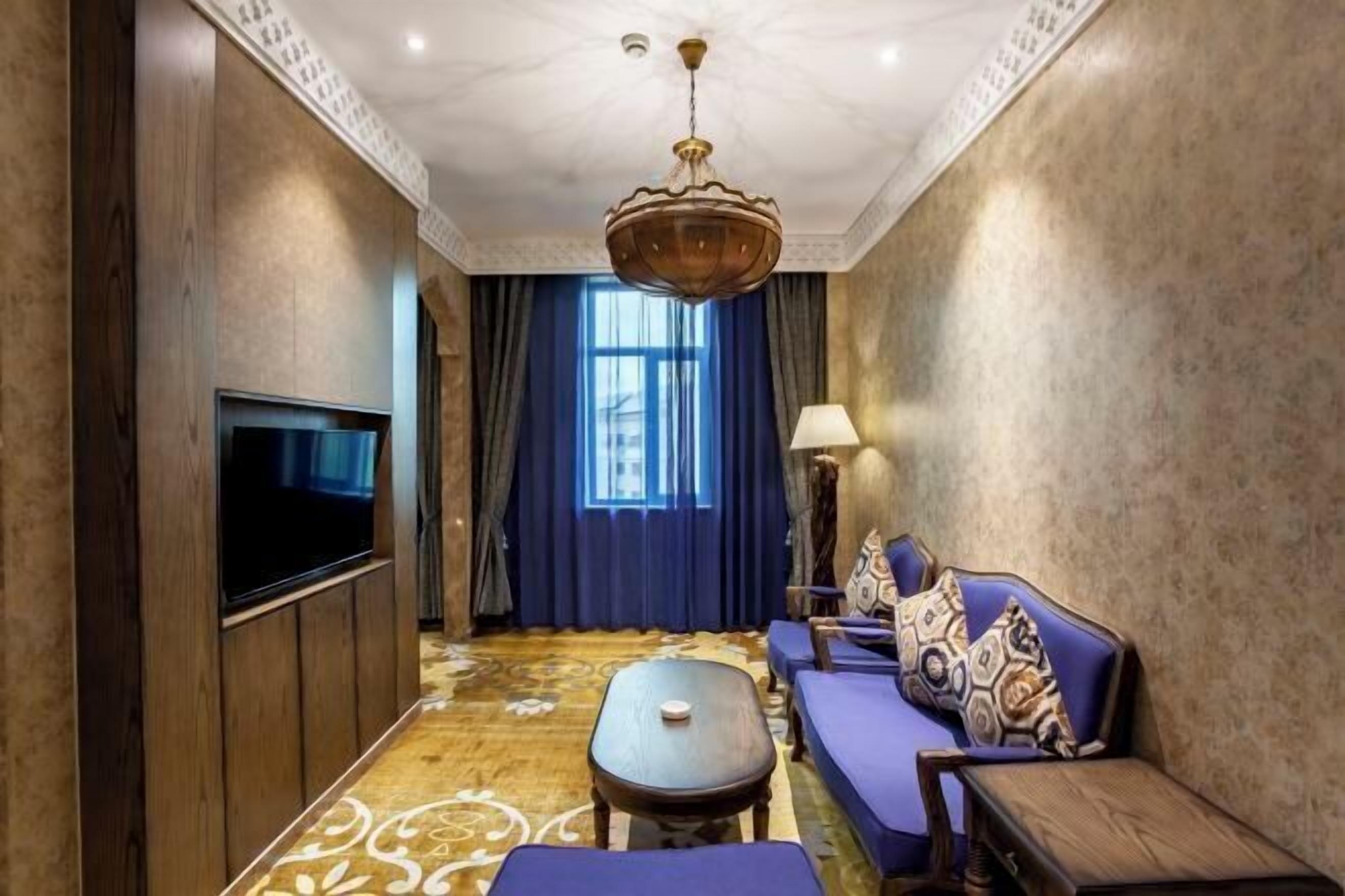 A hotel room with a TV, sofa, lamp, and patterned carpet.