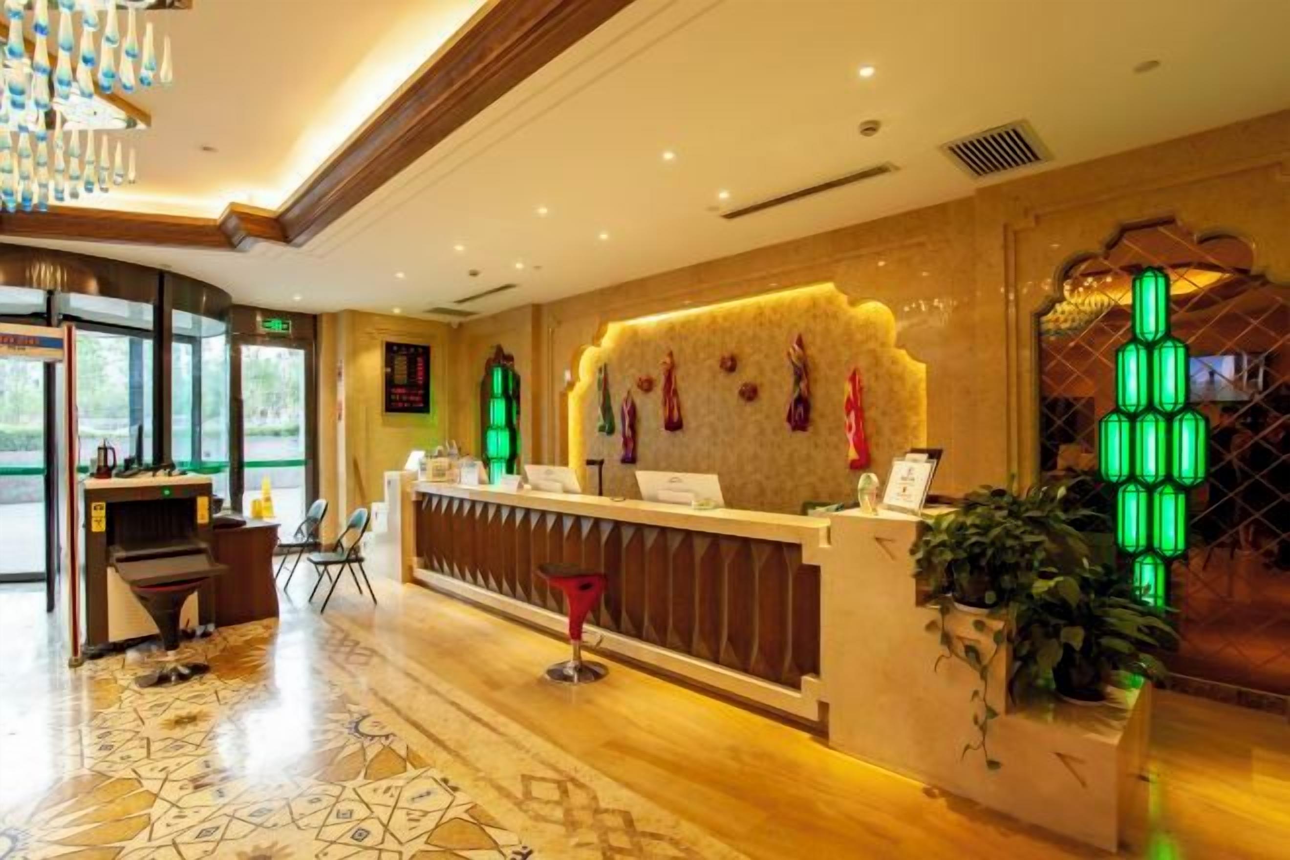 A hotel reception area with a modern design, including a patterned floor, a reception desk, and a green-lit wall decoration.
