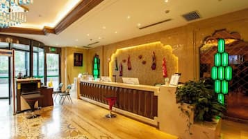 A hotel reception area with a modern design, including a patterned floor, a reception desk, and a green-lit wall decoration.