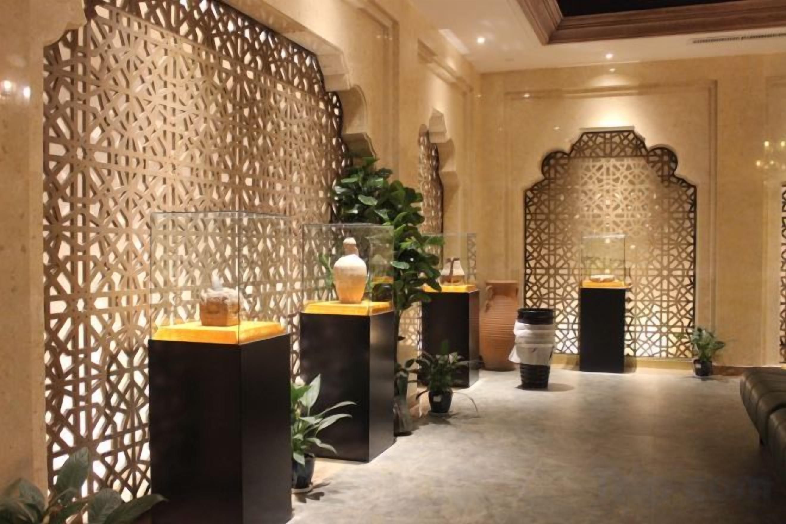 Un pasillo con paneles decorativos, plantas en macetas y un mostrador de recepción con un jarrón.