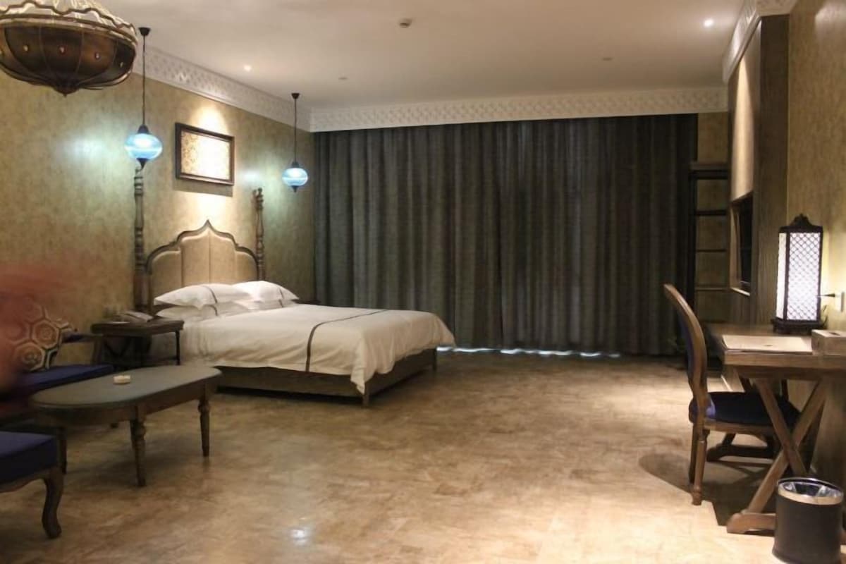 Una habitación de hotel con cama, escritorio, silla, mesa y cortina.