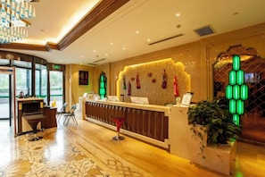 A hotel reception area with a reception desk, a seating area, and a large window. - Konghe Yizhan Culture Hotel (Turpan)