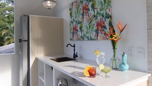 Una cocina moderna con encimera blanca, grifo negro, un cuadro de un pájaro colorido, un jarrón con flores y una rodaja de fruta sobre la encimera.