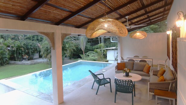 Un área junto a la piscina con asientos, una mesa y luces colgantes.