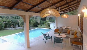 Un espace aménagé au bord de la piscine, avec des sièges, une table et des guirlandes lumineuses.