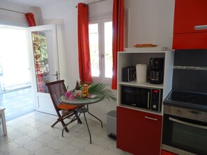 Une cuisine équipée d’une table à manger, de chaises, d’un four à micro-ondes, d’une machine à café et d’un meuble rouge.