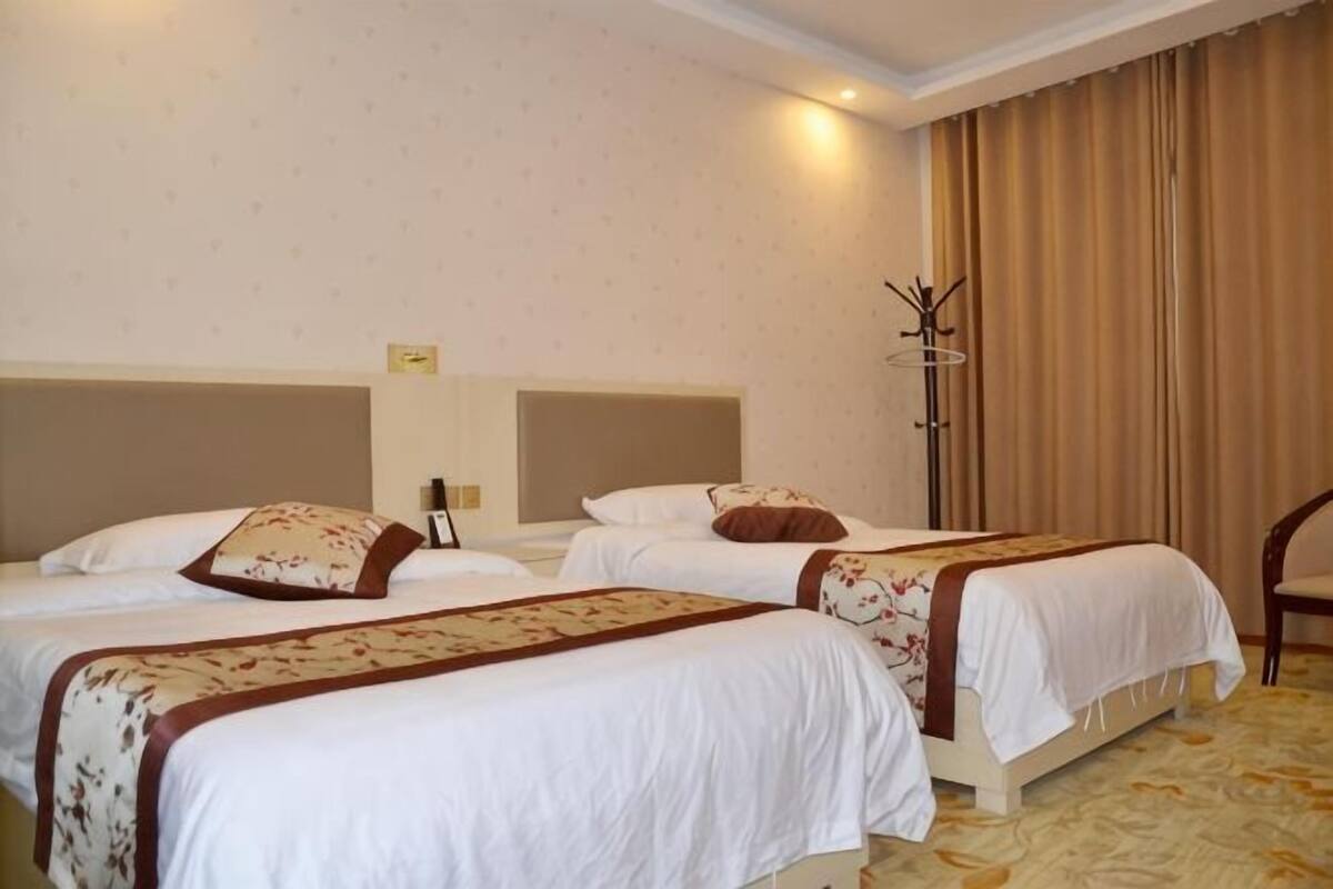 A hotel room with two beds, a nightstand, a lamp, and a chair.